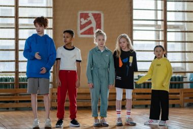 A diverse group of children in a sports hall preparing for an activity, showcasing teamwork and joy.